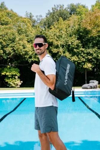 Atleta sorridente con occhiali da sole a bordo piscina mentre trasporta a tracolla la borsa nera del sistema di pressoterapia Wepere VIGGO.