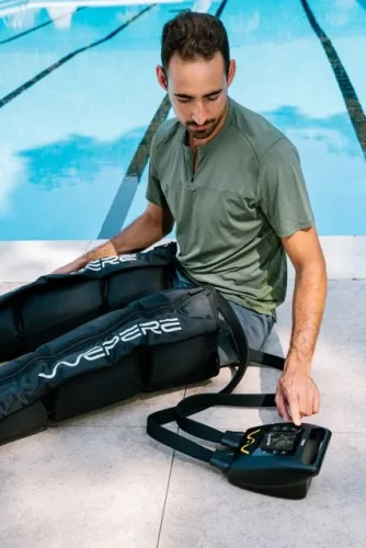 Atleta seduto a bordo piscina mentre imposta il dispositivo portatile di pressoterapia Wepere VIGGO collegato ai gambali per il recupero muscolare.