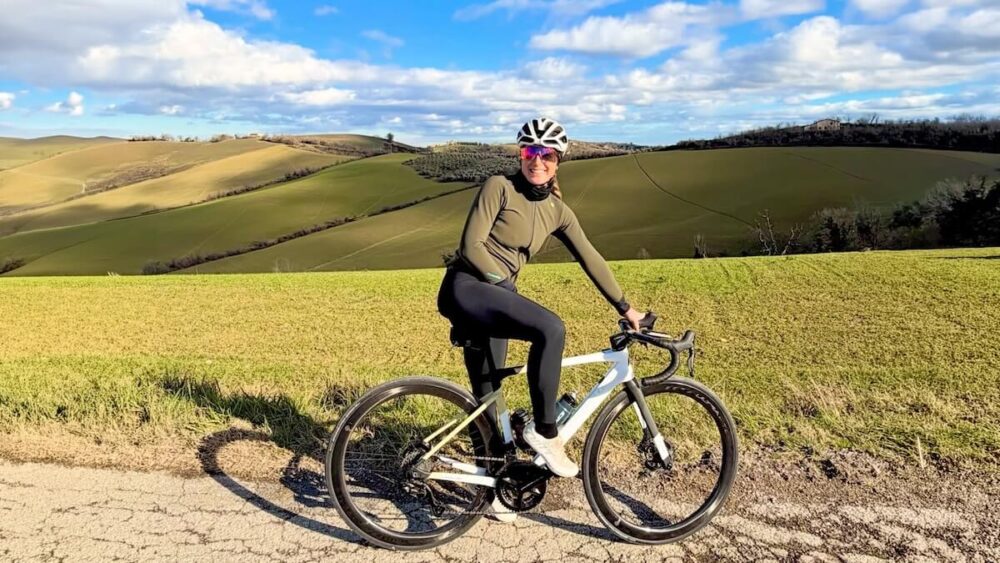Giorgia Bandini in sella alla sua bici da corsa su una strada collinare, ambassador WEPERE per il benessere muscolare nel ciclismo